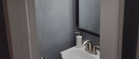 Un baño con lavamanos blanco, un espejo y un perchero para toallas.