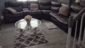 A living room with a sectional sofa, a glass coffee table, and a patterned rug. - Cozy 5-bdrm hm, Loaded Kitchen, w/ Patio 
Deck & Grill, WiFi in pleasant Norfolk (Norfolk)