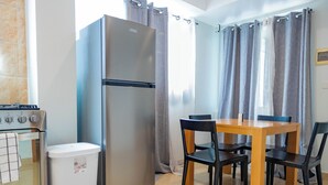 A compact kitchen with a stainless steel refrigerator, a small trash bin, and a wooden dining table with four chairs.