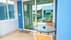 A balcony with a glass door leading to a terrace, a round glass table with a blue bowl, and a welcome mat.