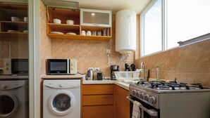 A compact kitchen with a washing machine, microwave, stove, and a water heater.