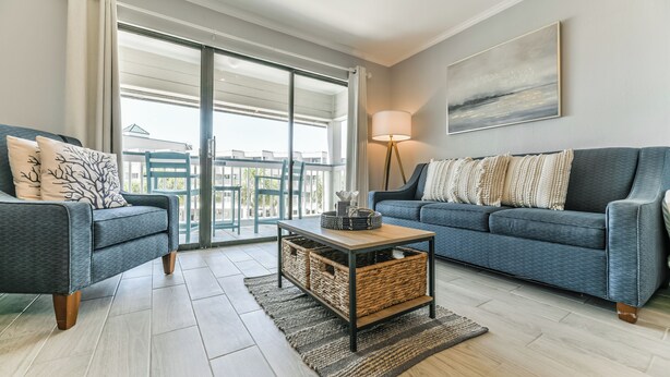 A modern living room with a sofa, a coffee table, and a view of a balcony. - La CaSEAta - Beachfront Condo (Galveston)