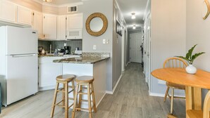 A kitchen with white cabinets, a granite countertop, and a wooden dining table with two stools. - La CaSEAta - Beachfront Condo (Galveston)
