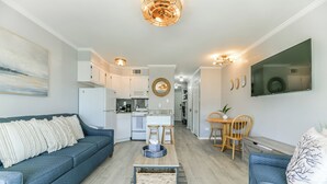 A modern living room with a sofa, coffee table, and a dining area with a table and chairs. - La CaSEAta - Beachfront Condo (Galveston)