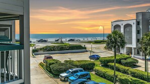 A parking area with several cars, a statue, and a view of the ocean at sunset. - La CaSEAta - Beachfront Condo (Galveston)