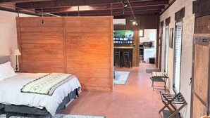 Ein gemütliches Zimmer mit Holzbalkendecke, einem Bett mit gemustertem Überwurf, einer Bank und einem Fernseher im Hintergrund.