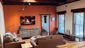 Ein gemütliches Wohnzimmer mit Holzbalkendecke, Kamin, Sofa, Couchtisch und Wand-Fernseher.