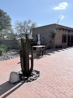A courtyard with a cactus, a table with an umbrella, and a brick building.