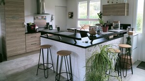 A modern kitchen with a central island, bar stools, and potted plants. - Quiet house (Bournainville-Faverolles)