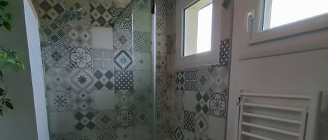 Un baño con baldosas estampadas, cabina de ducha de vidrio, un ventanal pequeño y un radiador blanco.