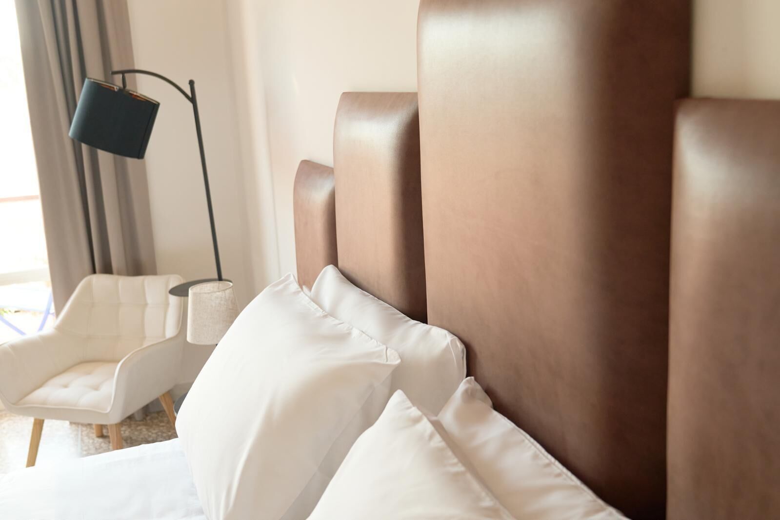 Een hotelkamer met een groot bed, witte kussens, een moderne stoel en een vloerlamp.