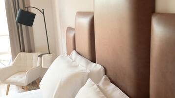 Een hotelkamer met een groot bed, witte kussens, een moderne stoel en een vloerlamp.