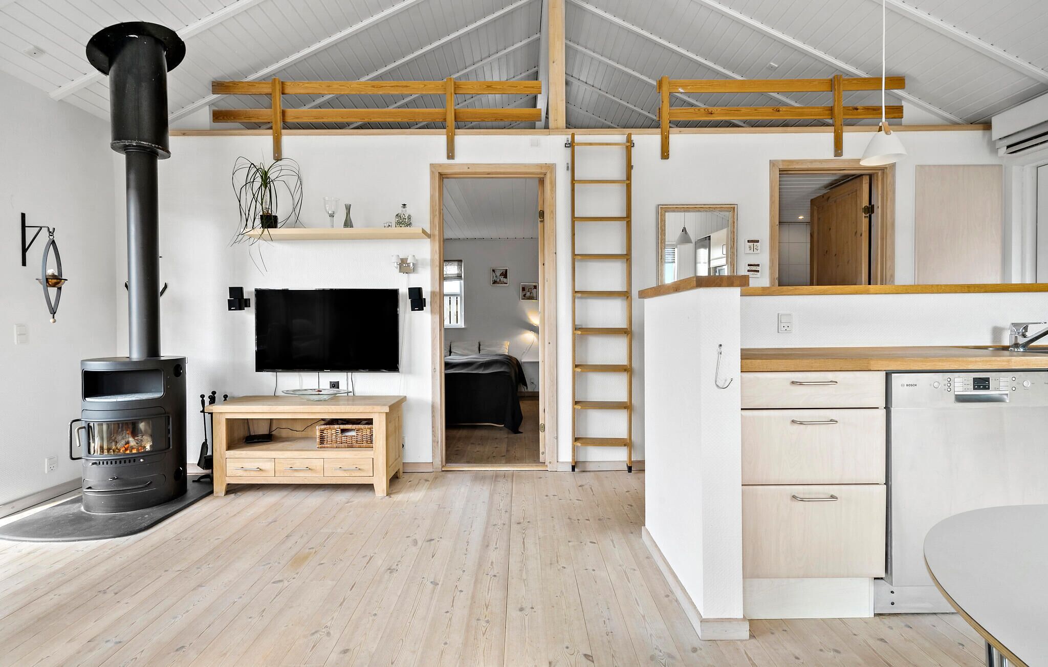 A modern, open-plan living space with a wood-burning stove, a flat-screen TV, and a kitchen area with a Bosch dishwasher.
