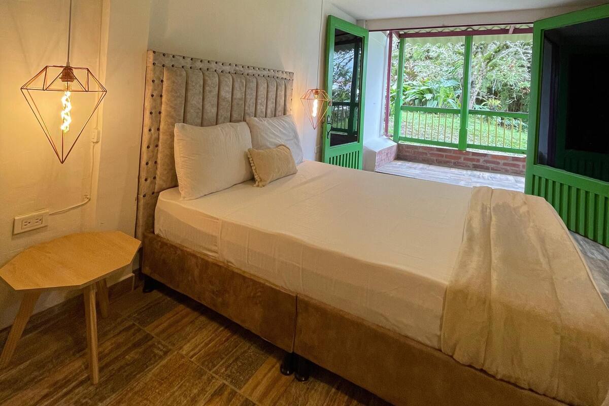 Une chambre avec un grand lit, une petite table et une fenêtre donnant sur un paysage verdoyant.