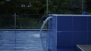 En swimmingpool med klart vatten, en blå kakelbeklädd vägg och ett metallräcke.