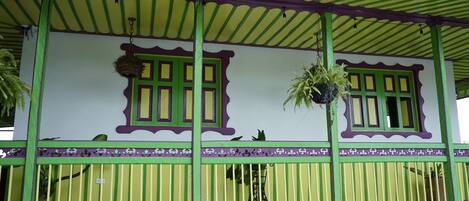 Un edificio con fachada verde y amarilla, ventanas grandes con detalles morados y plantas colgantes.