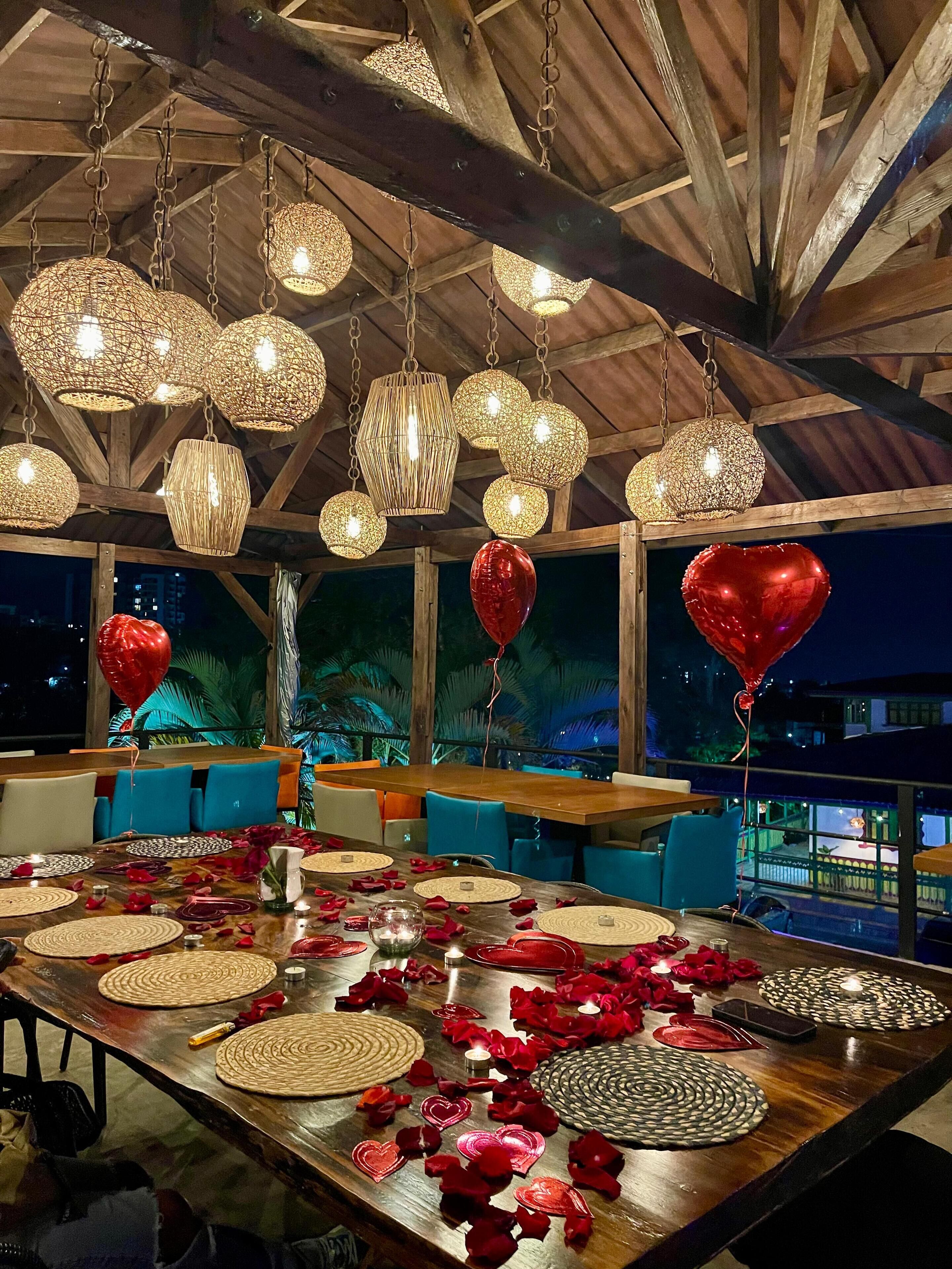 A dining area with a wooden table set for two, surrounded by blue chairs, under a wooden ceiling with hanging light fixtures.
