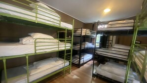 Dormitori amb lliteres disposades en dues files, sòl de fusta i una finestra que deixa entrar llum natural.