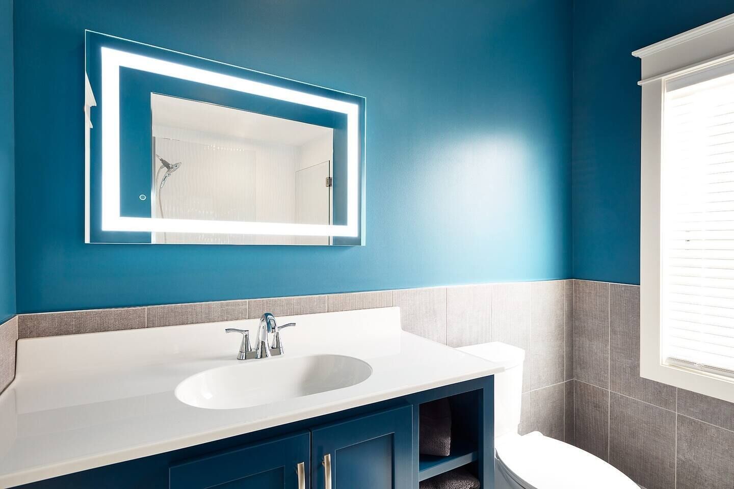 A bathroom with a white sink, blue cabinets, and a mirror with illuminated edges.