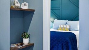 A bedroom with a blue headboard, a bed with blue bedding, and a nightstand with a plant and decorative items. - Pickwick Places 201 MSU/Rountree (Springfield)