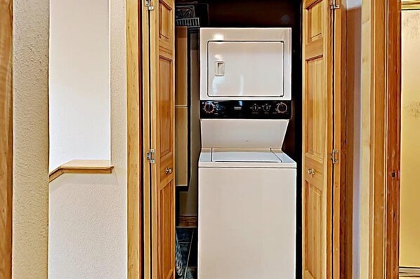 Une cuisine compacte dotée d’un four et d’un micro-ondes encastrés, de meubles en bois et d’un petit réfrigérateur.