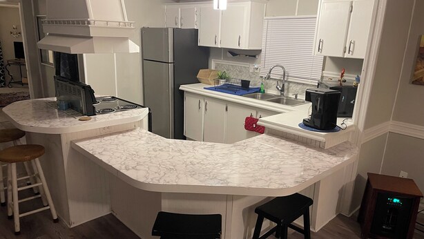 A modern kitchen with white cabinetry, a built-in stove, and a marble countertop. There are two stools and a coffee machine. - 3/2 Sunken Treasure Spacious Home in college town of Troy with WiFi, AC (Troy)