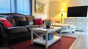 A living room with a brown leather sofa, a white coffee table, a red rug, a television, and a lamp. - 3/2 Sunken Treasure Spacious Home in college town of Troy with WiFi, AC (Troy)