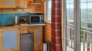 A compact kitchen with a microwave, kettle, and small refrigerator. There are wooden cabinets and a window with a view. - Brockalee Farm Retreat (Bardon Mill, Near Hexham)