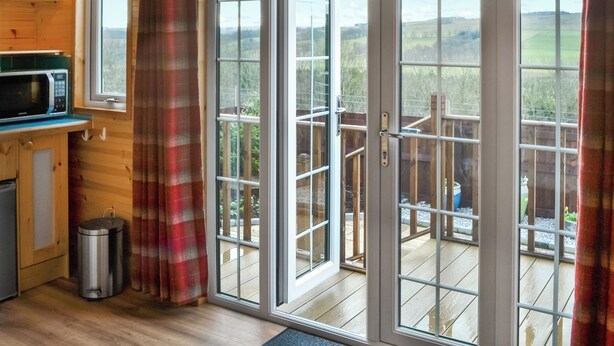 A wooden interior with a kitchen area, a sliding glass door leading to a deck, and a view of the outdoors. - Brockalee Farm Retreat (Bardon Mill, Near Hexham)