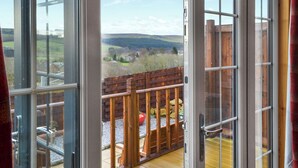 A view from a room with large glass doors leading to an outdoor deck with a wooden railing and a view of the countryside. - Brockalee Farm Retreat (Bardon Mill, Near Hexham)