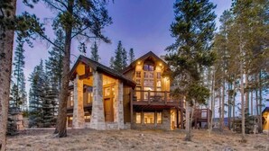 A large, multi-story log cabin with a stone foundation, surrounded by tall pine trees. - Breck_snowy_point_chalet (Breckenridge)