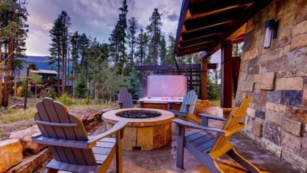 An outdoor seating area with Adirondack chairs and a fire pit, surrounded by stone walls and a wooden pergola. - Breck_summit_at_shockhill (Breckenridge)