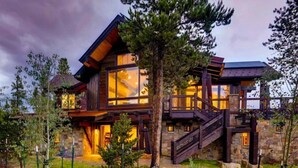 Una cabaña moderna de troncos con ventanas amplias, base de piedra y una escalera de madera que conduce a la entrada.