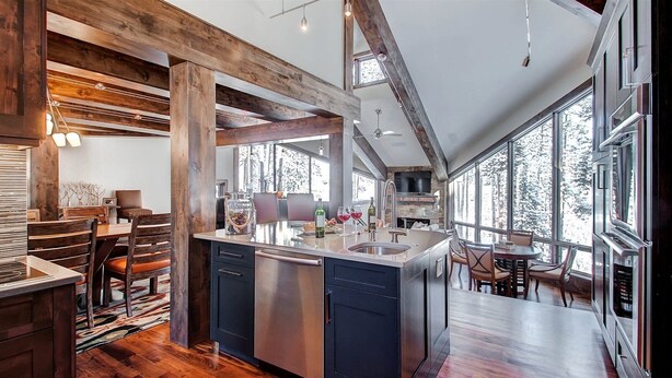 A spacious kitchen with a central island, wooden beams, large windows, and a stone fireplace. - Breck_grand_vista_lodge (Breckenridge)