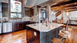 A modern kitchen with a central island, wooden beams, and a dining area with stools. - Breck_grand_vista_lodge (Breckenridge)
