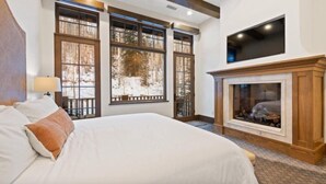 A bedroom with a large bed, a fireplace, and large windows with a view of trees. - Vail_alpenzauber_lodge_5bd (Vail)