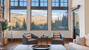 A living room with a large window view of a mountainous landscape, two armchairs, a coffee table, and a lamp. - Vail_alpenzauber_lodge_5bd (Vail)