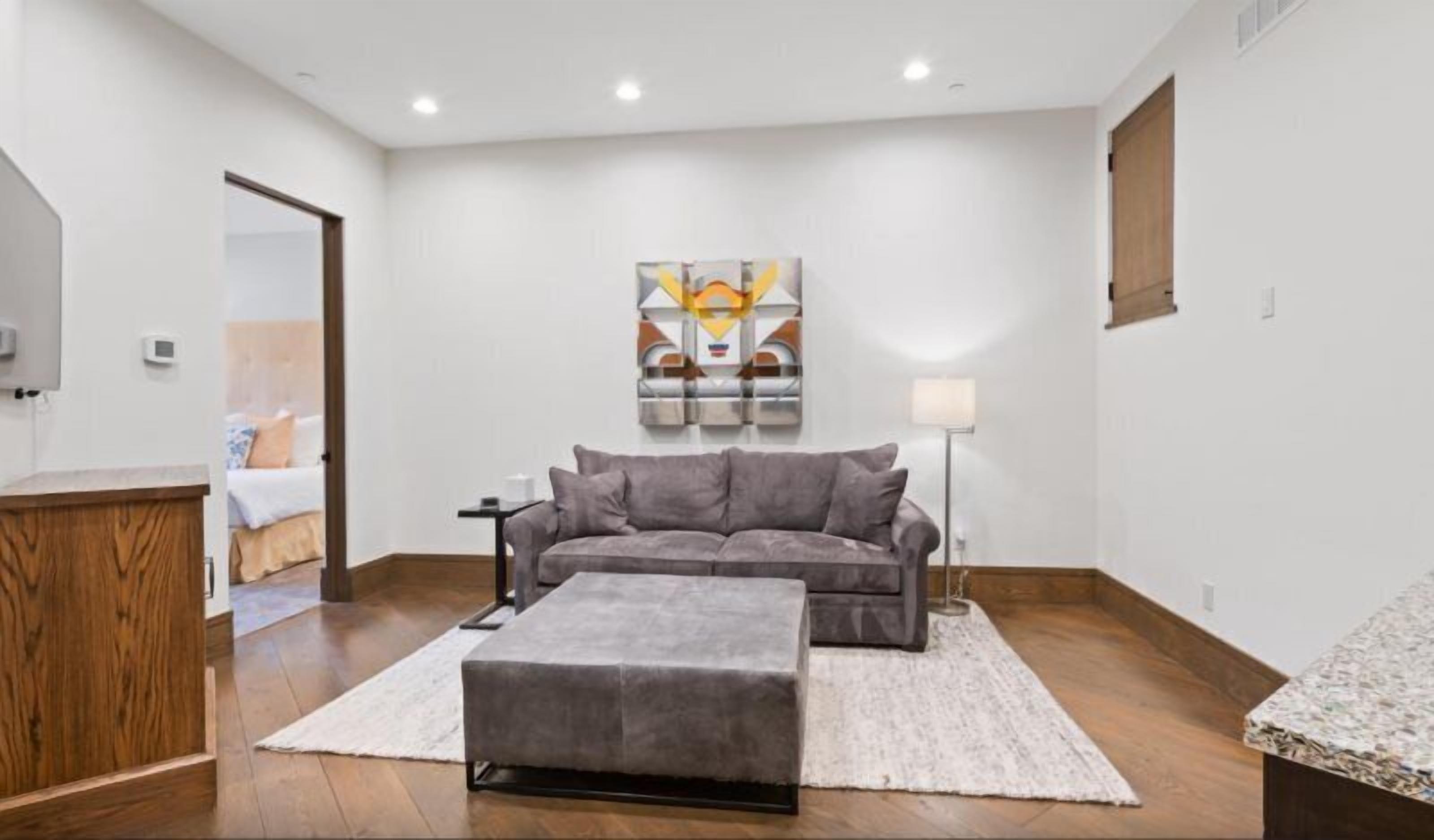 Un salon moderne avec un canapé gris, un petit pouf, une lampe sur pied et un tableau accroché au mur.
