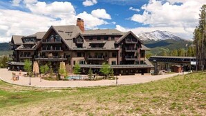 A large, multi-story lodge with a prominent chimney, balconies, and a view of a snow-capped mountain. - Crystal Peak 2 Bedroom Condo at Peak 7 (Breckenridge)