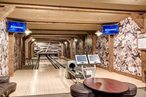 A bowling alley with wooden walls and ceiling, two screens displaying 'Brunswick', and a seating area with a table and stools. - Crystal Peak 2 Bedroom Condo at Peak 7 (Breckenridge)