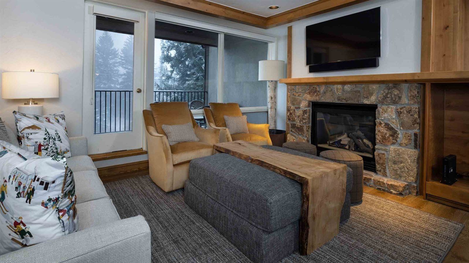 A cozy living room with a stone fireplace, comfortable seating, and a television mounted above it.