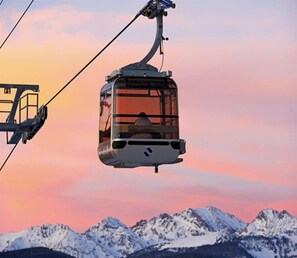 A cable car suspended over a mountainous landscape with a sunset in the background. - Vail Village Gravity Haus 2 Bedroom Condo (Vail)