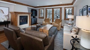 Una sala de estar acogedora con sofás de cuero, chimenea y un ventanal con vistas a árboles nevados.