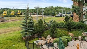 A hotel with a view of a cable car system, a well-maintained lawn, and outdoor seating area. - Snowmass_village_3bd_gen_c (Snowmass Village)