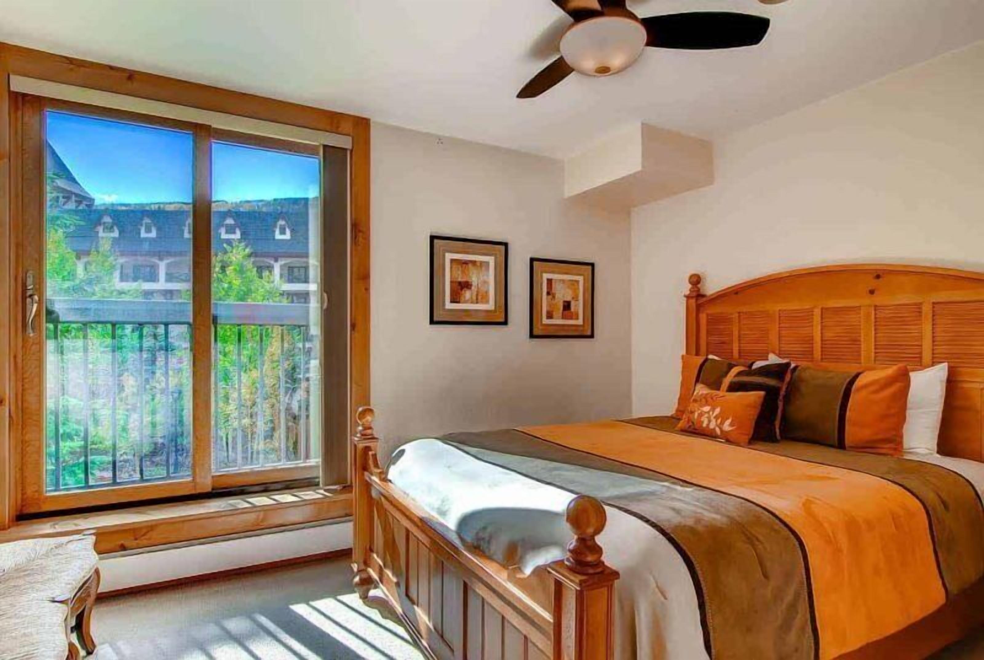 A bedroom with a large window, a bed with an orange bedspread, and two framed pictures on the wall.