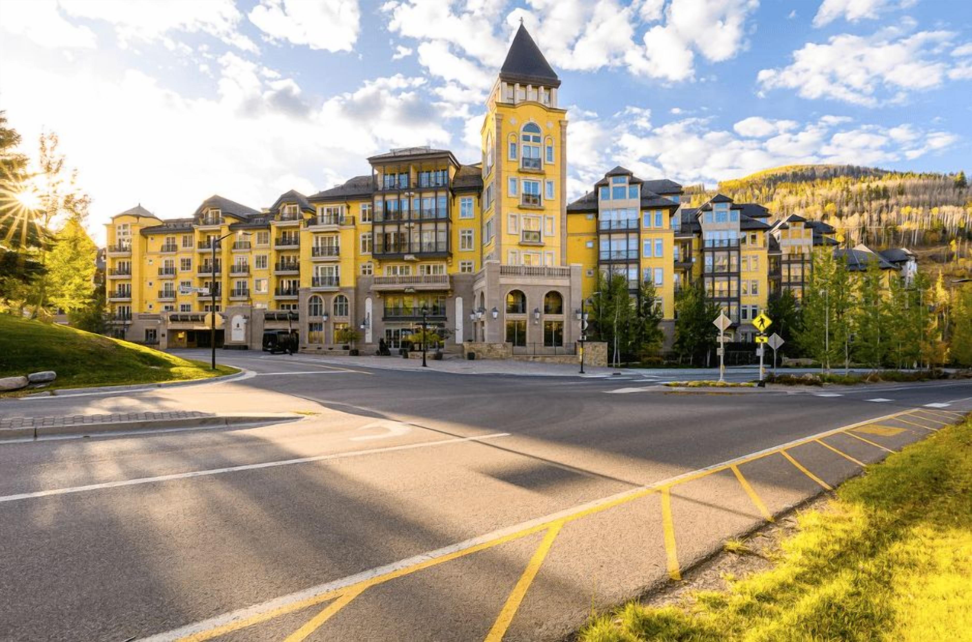 A multi-story hotel with a central tower, a parking lot, and a hilly landscape in the background.
