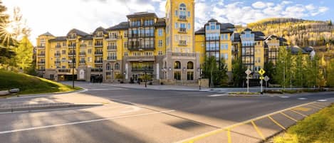 A multi-story hotel with a central tower, a parking lot, and a hilly landscape in the background.