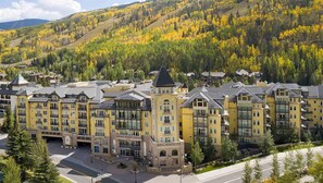Un hotel a più piani con un cortile centrale, circondato da alberi dai colori autunnali e uno sfondo montuoso.
