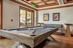 A pool table in a room with wooden flooring, a bench, and two framed artworks on the wall.
