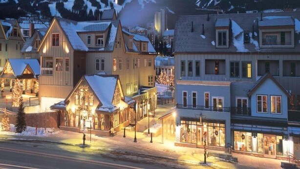 Eine verschneite Bergstadt im Abendlicht mit traditionellen Holzhäusern und freiem Blick auf die Berge.